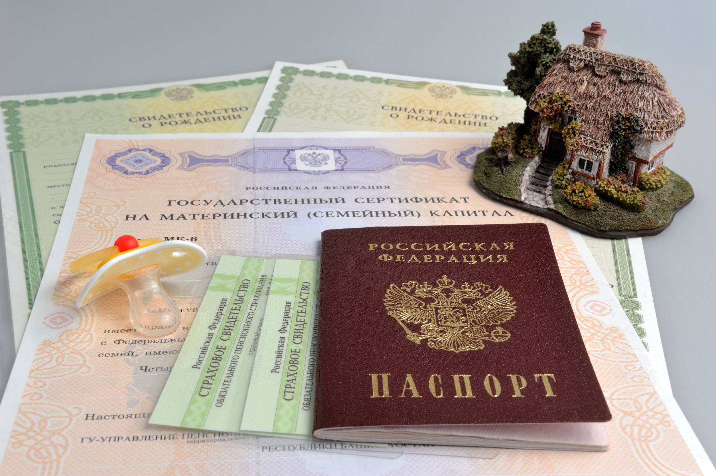 Passport with baby dummy model of house and maternal birth and pension certificates