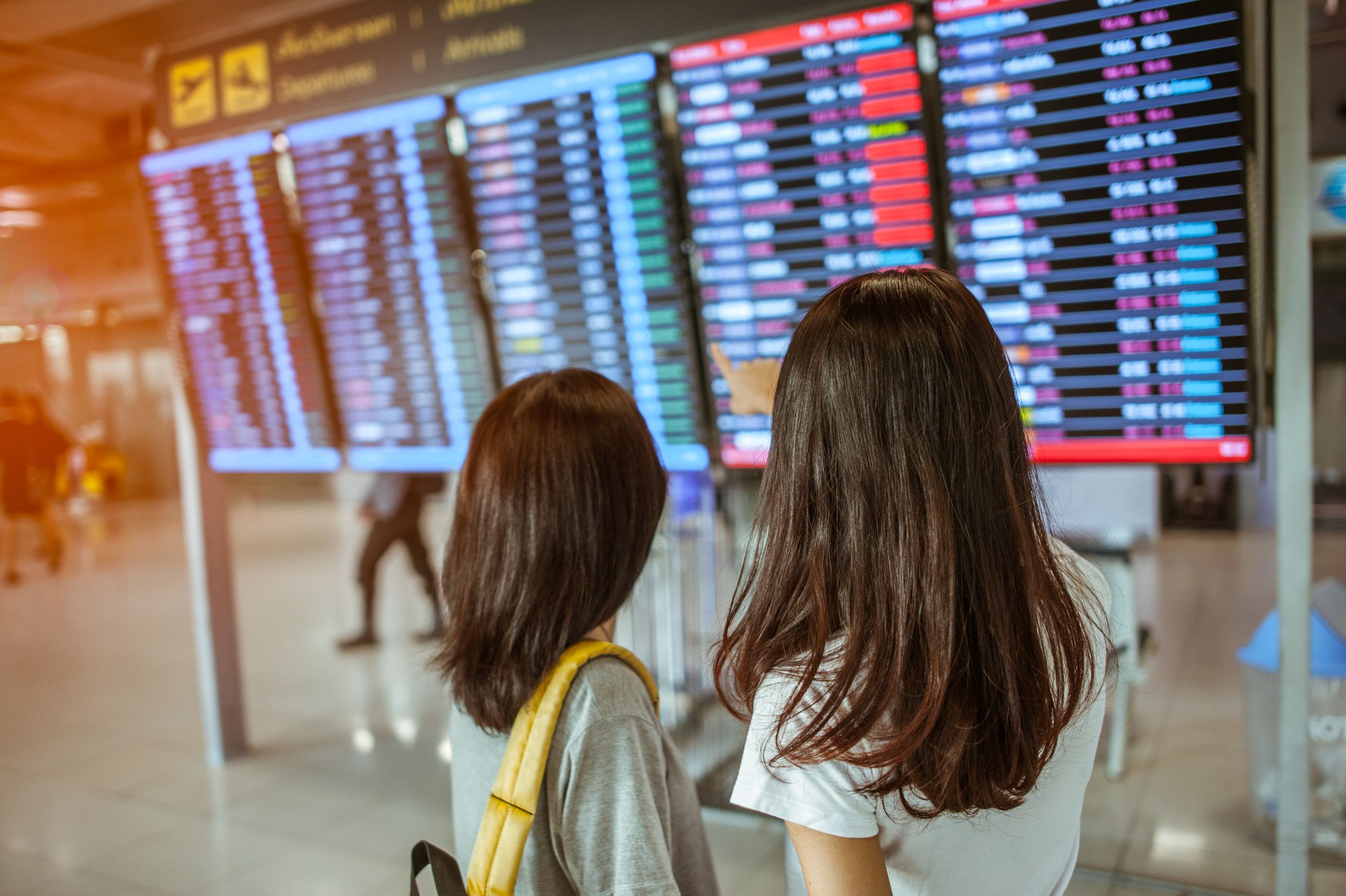 Two women in international airport terminal looking at information board checking